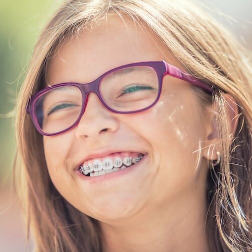 Portrait of a happy smiling teenage girl with dental braces and glasses.