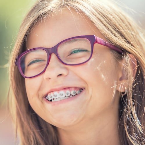 Portrait of a happy smiling teenage girl with dental braces and glasses.